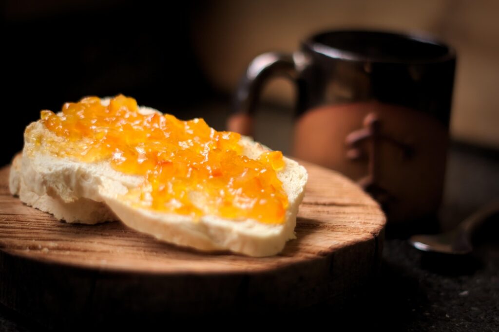 Slice of bread topped with marmalade served with a coffee mug in a cozy breakfast setting